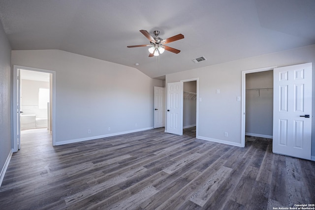 unfurnished bedroom featuring dark wood-type flooring, a walk in closet, vaulted ceiling, and ceiling fan