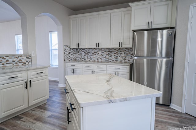 kitchen featuring white cabinetry, a center island, stainless steel fridge, and light stone counters