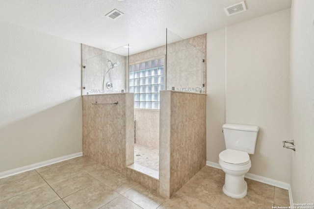 bathroom with tiled shower, toilet, tile patterned flooring, and a textured ceiling