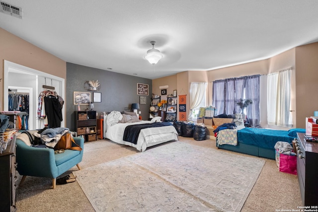 bedroom with ceiling fan, light colored carpet, a closet, and a walk in closet