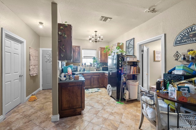 kitchen featuring black refrigerator, light tile patterned flooring, a textured ceiling, and a notable chandelier