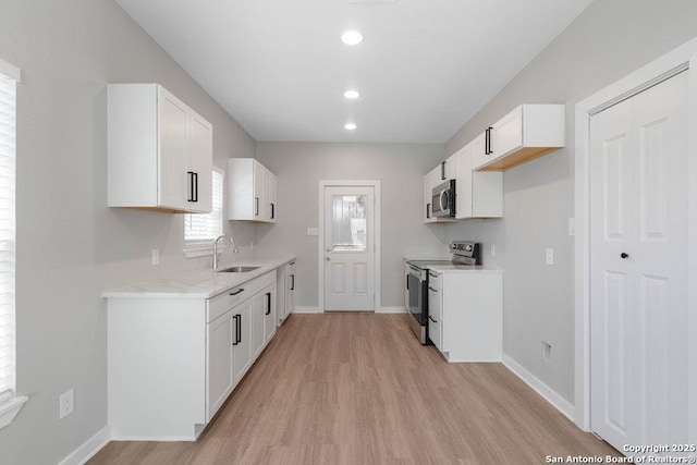 kitchen with sink, appliances with stainless steel finishes, light stone counters, light hardwood / wood-style floors, and white cabinets