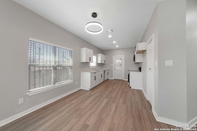 kitchen featuring white cabinetry, sink, decorative light fixtures, and light wood-type flooring