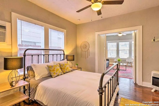 bedroom with dark hardwood / wood-style floors, heating unit, and ceiling fan