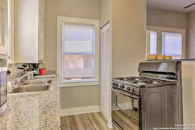 kitchen with white cabinetry, sink, light stone counters, gas stove, and light hardwood / wood-style flooring