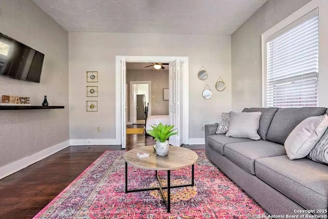 living room featuring dark hardwood / wood-style flooring, ceiling fan, and a textured ceiling