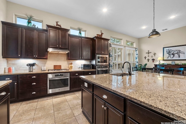 kitchen with stainless steel appliances, light stone countertops, sink, and decorative light fixtures