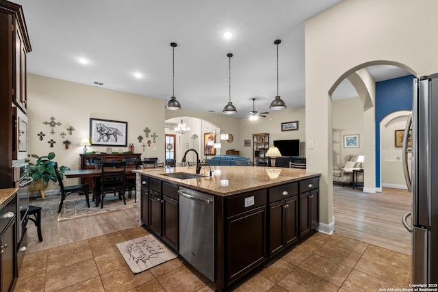 kitchen with appliances with stainless steel finishes, decorative light fixtures, sink, light stone counters, and dark brown cabinetry