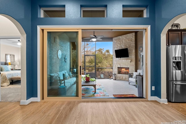 doorway to outside with a stone fireplace, wood-type flooring, and ceiling fan