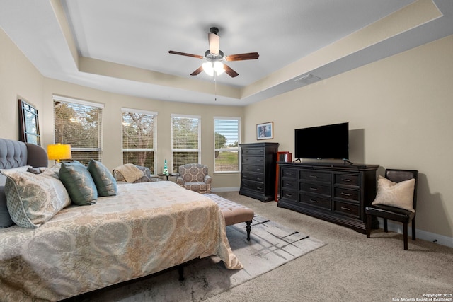 bedroom with ceiling fan, a tray ceiling, and light carpet