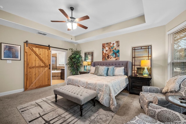 carpeted bedroom featuring ceiling fan, ensuite bathroom, a barn door, and a raised ceiling