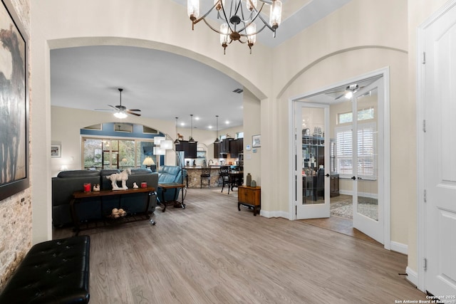 foyer entrance with french doors, ceiling fan with notable chandelier, and light wood-type flooring