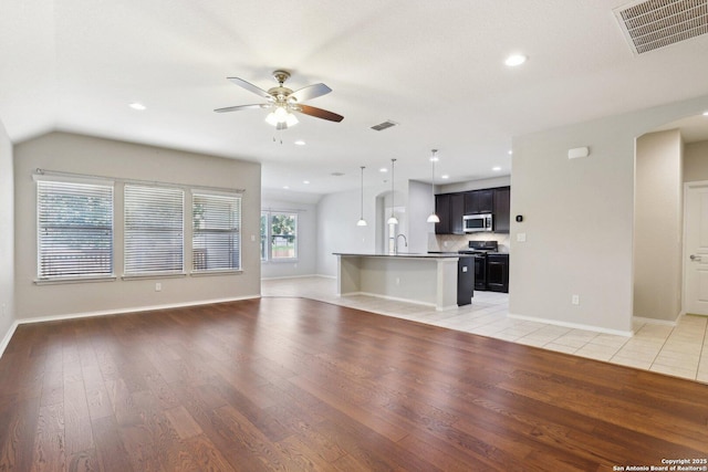 unfurnished living room with vaulted ceiling, ceiling fan, sink, and light hardwood / wood-style floors