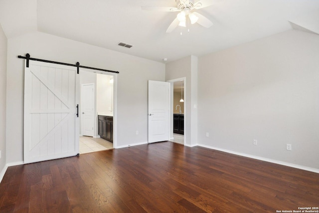 unfurnished bedroom featuring vaulted ceiling, ensuite bathroom, wood-type flooring, ceiling fan, and a barn door