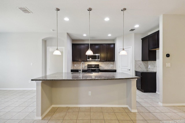 kitchen with sink, range, dark stone countertops, light tile patterned floors, and a kitchen island with sink