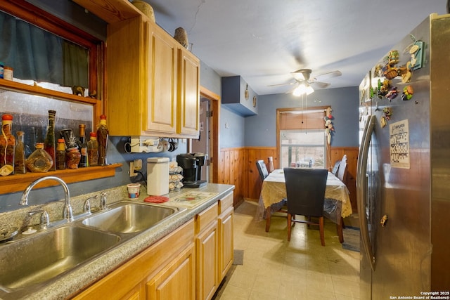 kitchen featuring stainless steel refrigerator, ceiling fan, wooden walls, and sink