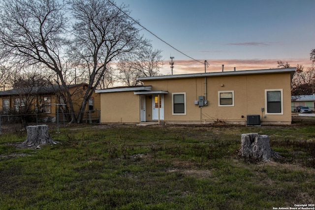 back house at dusk with cooling unit and a lawn