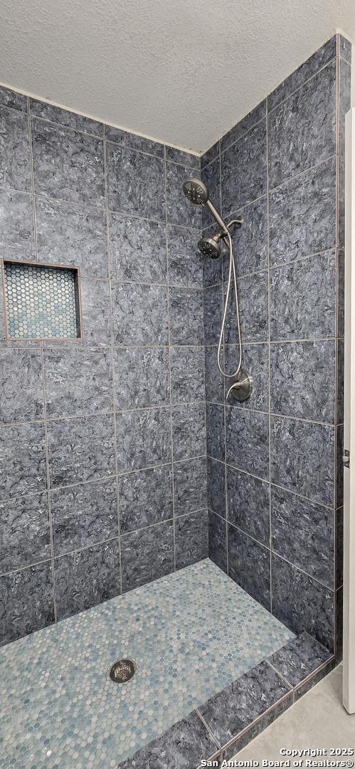 bathroom featuring tile patterned flooring, a tile shower, and a textured ceiling