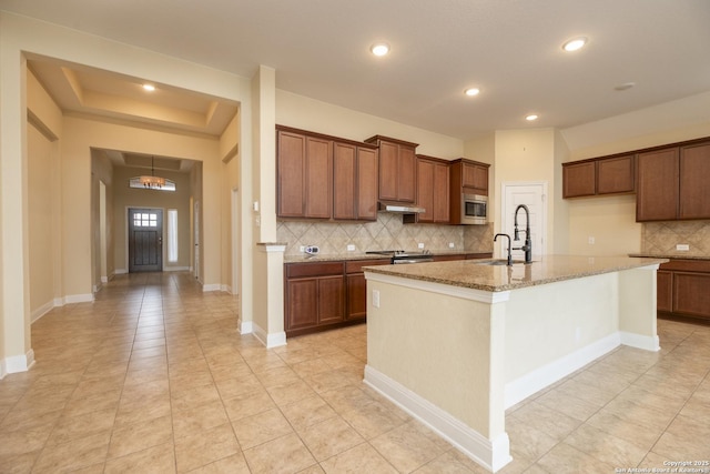 kitchen with sink, stainless steel appliances, light stone counters, an island with sink, and decorative backsplash