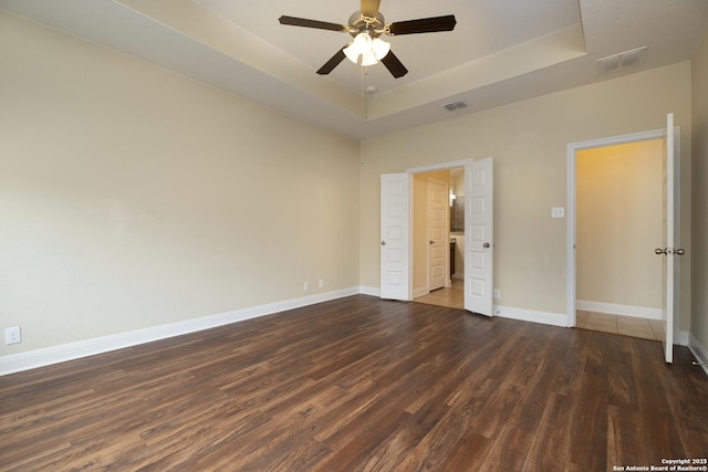 unfurnished bedroom with dark hardwood / wood-style flooring, a tray ceiling, and ceiling fan