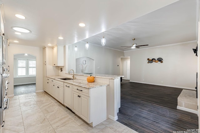 kitchen featuring sink, light stone counters, ornamental molding, kitchen peninsula, and white cabinets