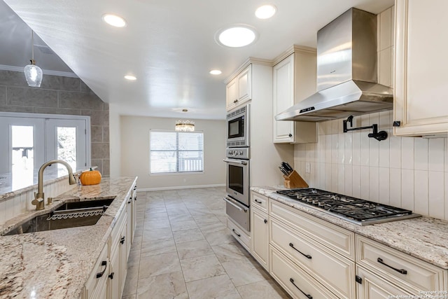 kitchen with wall chimney range hood, light stone countertops, sink, and appliances with stainless steel finishes