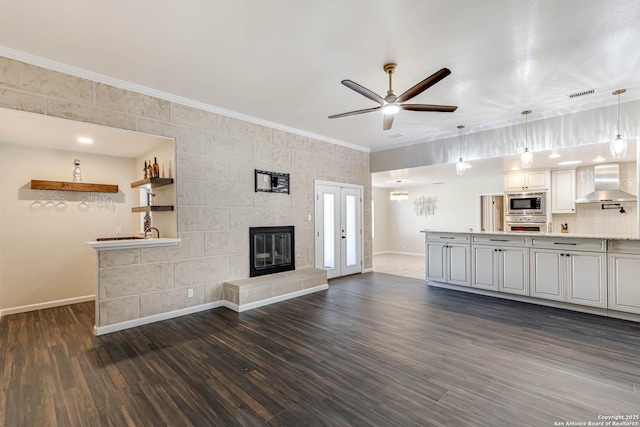 unfurnished living room with crown molding, ceiling fan, a tiled fireplace, bar area, and dark hardwood / wood-style flooring