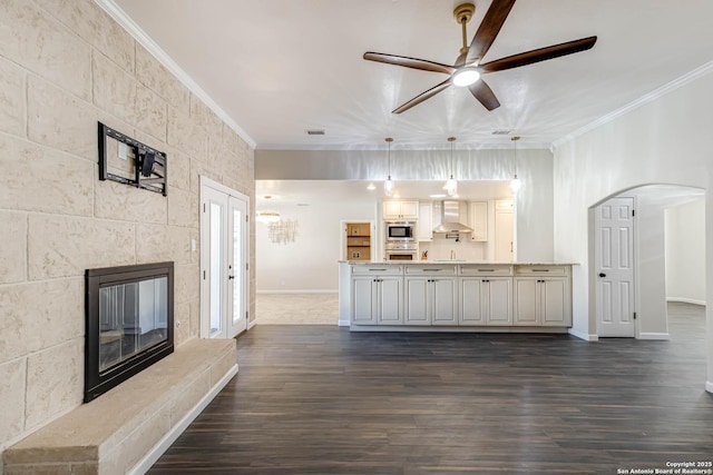 unfurnished living room featuring a tiled fireplace, dark wood-type flooring, ornamental molding, and ceiling fan