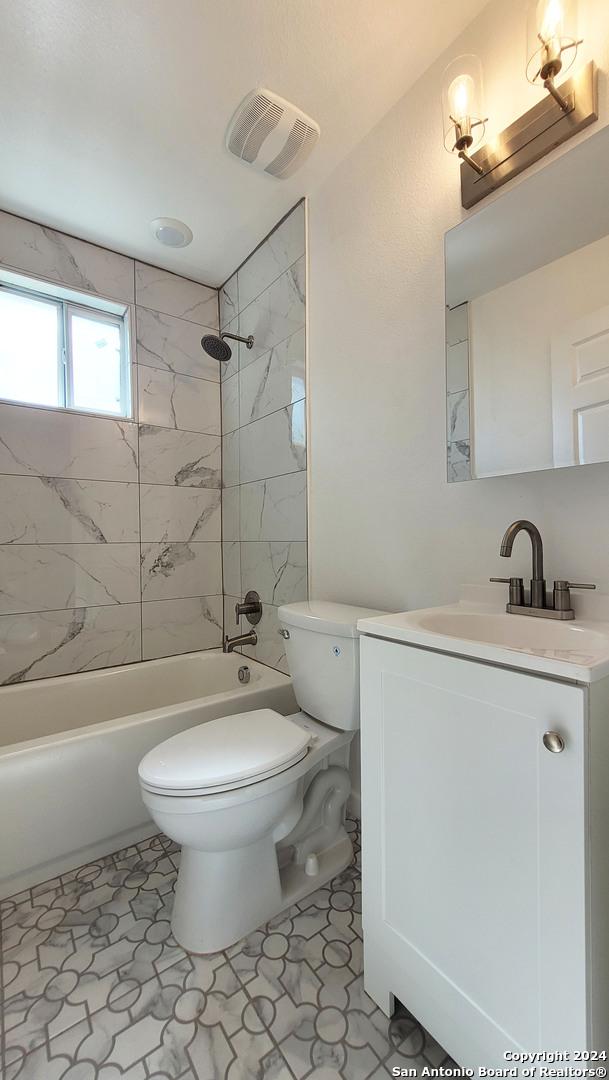 full bathroom with tile patterned flooring, tiled shower / bath, vanity, and toilet