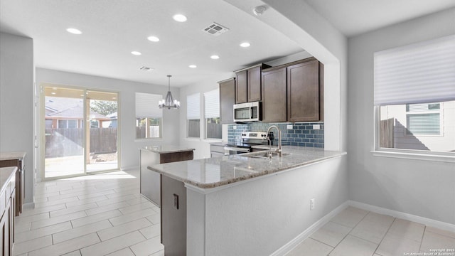 kitchen featuring tasteful backsplash, appliances with stainless steel finishes, kitchen peninsula, pendant lighting, and light stone countertops