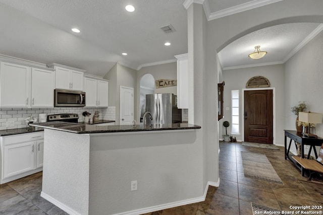 kitchen with dark stone countertops, backsplash, stainless steel appliances, ornamental molding, and white cabinets