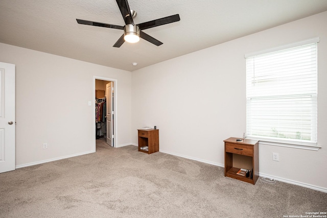 unfurnished bedroom featuring a spacious closet, light colored carpet, a closet, and ceiling fan