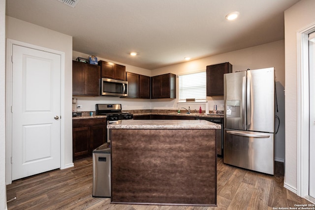 kitchen with sink, dark wood-type flooring, appliances with stainless steel finishes, dark brown cabinetry, and a kitchen island