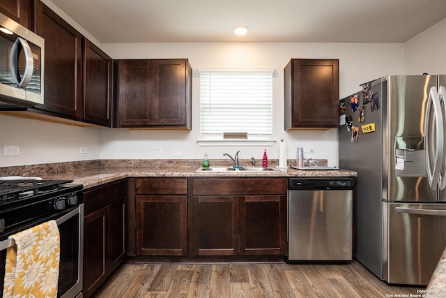 kitchen with appliances with stainless steel finishes, sink, dark hardwood / wood-style flooring, dark stone counters, and dark brown cabinets