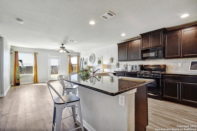 kitchen featuring sink, a breakfast bar area, light hardwood / wood-style floors, and black appliances