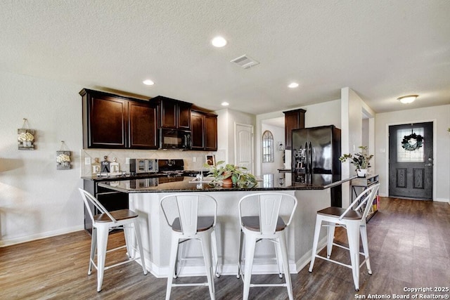 kitchen featuring a kitchen breakfast bar, wood-type flooring, black appliances, an island with sink, and decorative backsplash