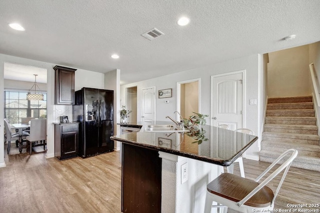 kitchen featuring sink, a kitchen island with sink, black refrigerator with ice dispenser, and a textured ceiling