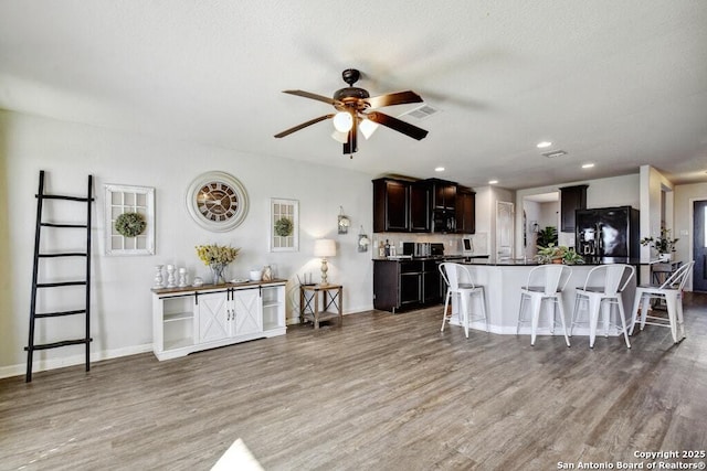 kitchen with a breakfast bar, a center island, light wood-type flooring, ceiling fan, and black appliances