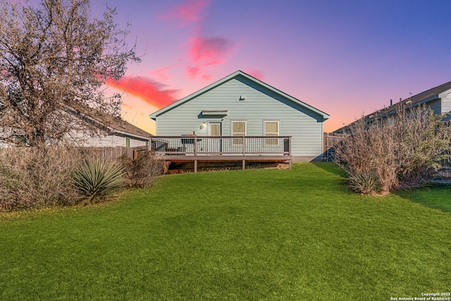 back house at dusk with a deck and a lawn