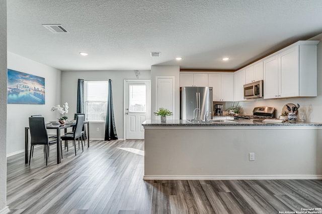 kitchen with stone countertops, white cabinets, light hardwood / wood-style floors, stainless steel appliances, and a textured ceiling