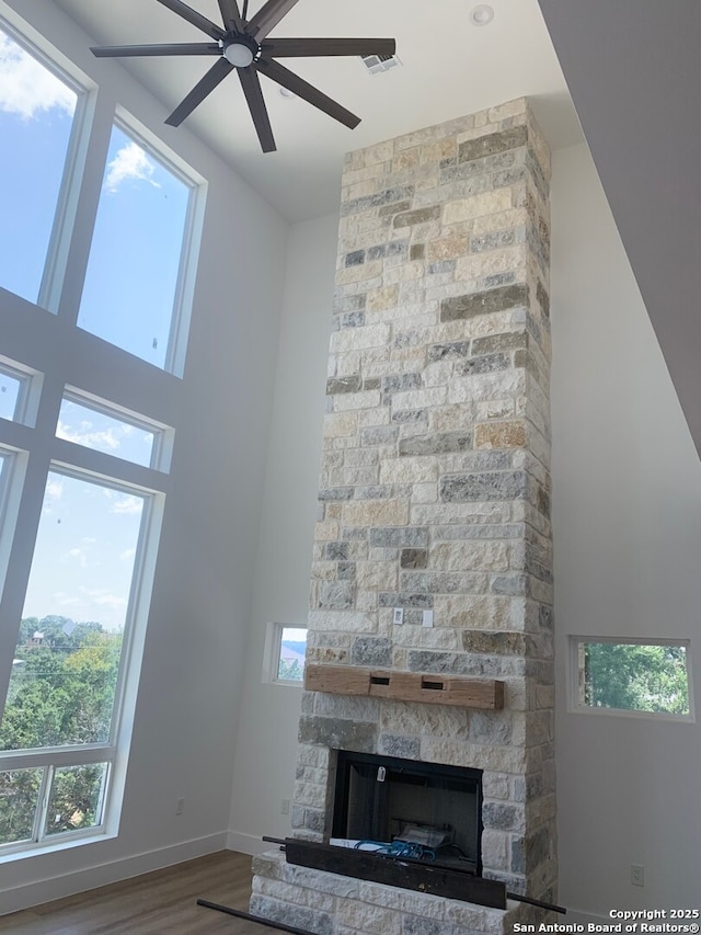 unfurnished living room featuring wood-type flooring, a stone fireplace, and ceiling fan