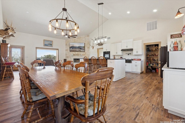 dining space with ceiling fan, high vaulted ceiling, dark wood-type flooring, and a fireplace