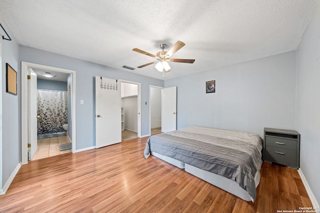 bedroom with connected bathroom, a textured ceiling, light hardwood / wood-style floors, and ceiling fan