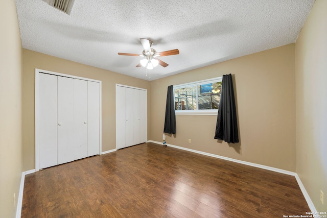 unfurnished bedroom featuring multiple closets, ceiling fan, dark wood-type flooring, and a textured ceiling