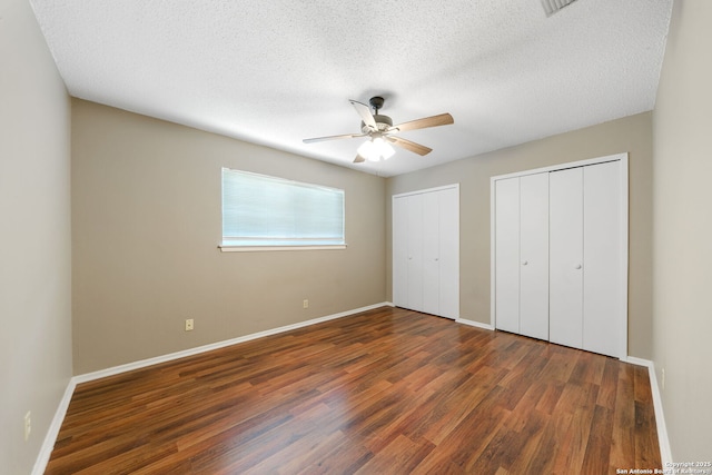 unfurnished bedroom featuring multiple closets, ceiling fan, dark hardwood / wood-style flooring, and a textured ceiling