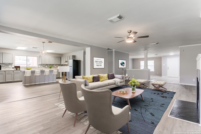 living room featuring crown molding, ceiling fan, light hardwood / wood-style floors, and ornate columns