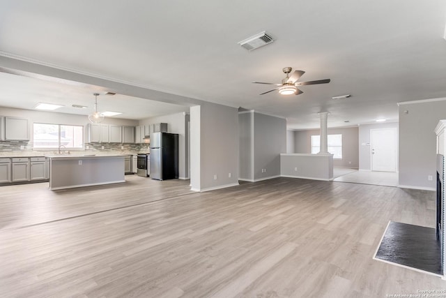 unfurnished living room with sink, crown molding, light hardwood / wood-style flooring, ceiling fan, and decorative columns