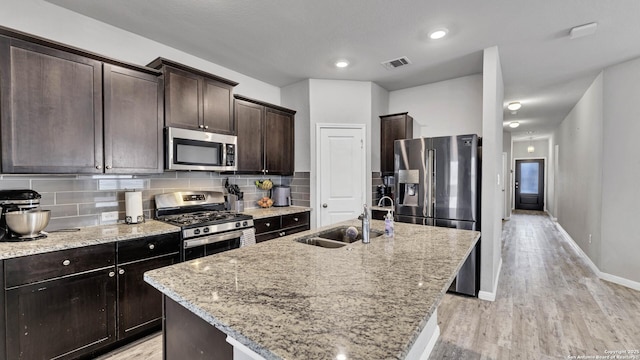 kitchen with light stone counters, sink, a center island with sink, and appliances with stainless steel finishes