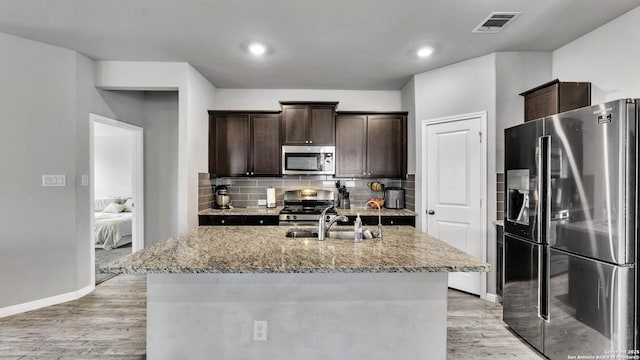 kitchen with light stone counters, appliances with stainless steel finishes, and an island with sink