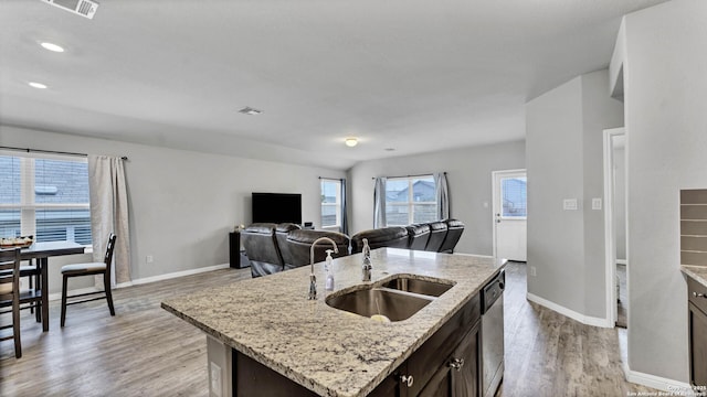 kitchen featuring dark brown cabinetry, sink, dishwasher, light stone countertops, and a kitchen island with sink